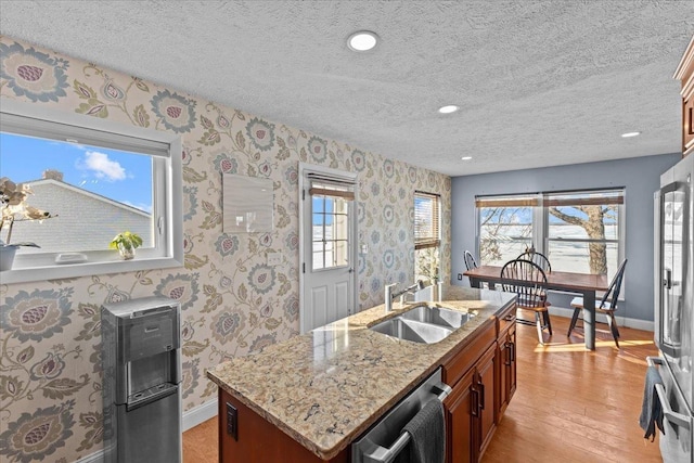 kitchen with stainless steel appliances, light hardwood / wood-style floors, a textured ceiling, sink, and an island with sink