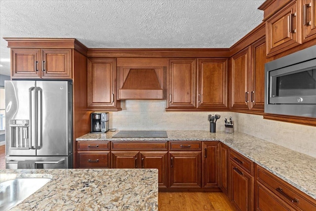 kitchen featuring wall chimney range hood, stainless steel appliances, light stone counters, and light hardwood / wood-style floors