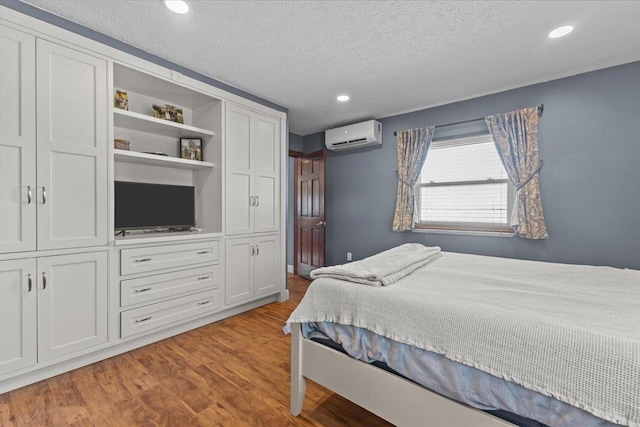 bedroom with a wall mounted air conditioner, a textured ceiling, and light wood-type flooring