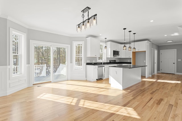 kitchen with hanging light fixtures, ornamental molding, a kitchen island, stainless steel appliances, and white cabinets