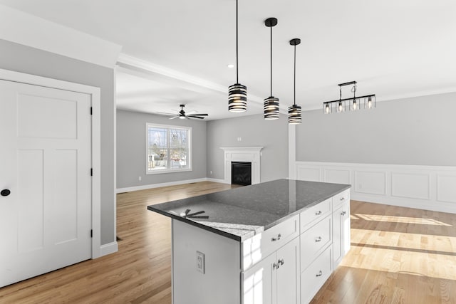 kitchen featuring a kitchen island, decorative light fixtures, white cabinetry, dark stone counters, and ceiling fan