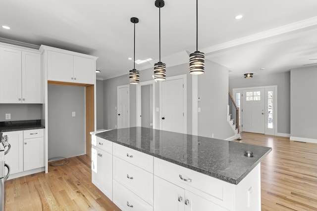 kitchen featuring light hardwood / wood-style flooring, a center island, white cabinets, decorative light fixtures, and dark stone counters