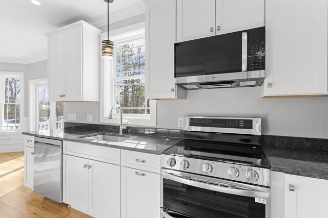 kitchen with sink, hanging light fixtures, light wood-type flooring, appliances with stainless steel finishes, and white cabinets