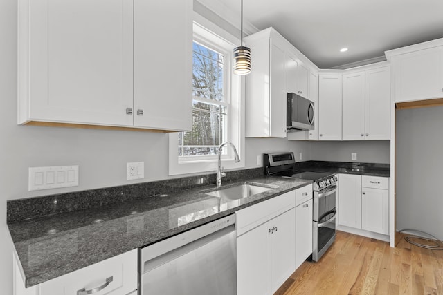 kitchen with sink, appliances with stainless steel finishes, dark stone countertops, hanging light fixtures, and white cabinets