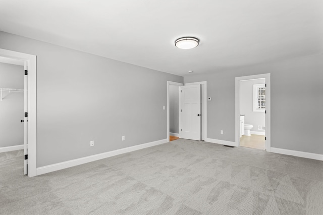 unfurnished bedroom featuring connected bathroom, light carpet, a closet, and a spacious closet