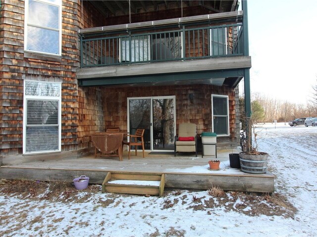 snow covered back of property with a wooden deck and a balcony