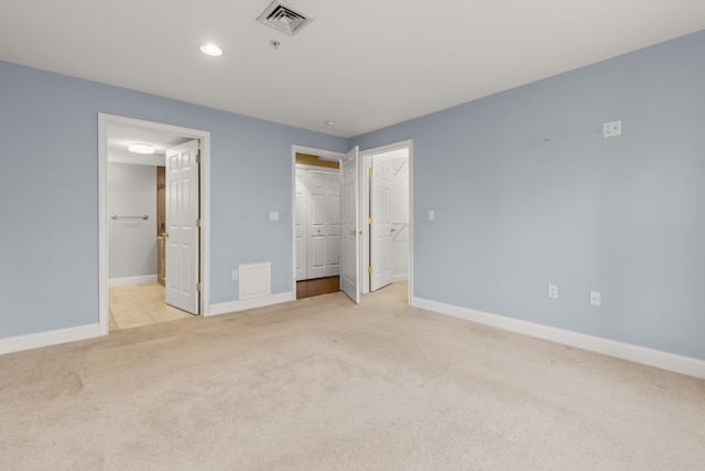 unfurnished bedroom with light colored carpet, a closet, and ensuite bath