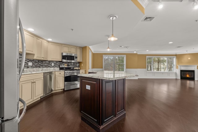 kitchen with cream cabinets, crown molding, decorative light fixtures, stainless steel appliances, and light stone counters