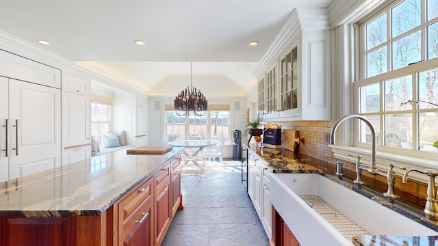 kitchen featuring sink, dark stone countertops, hanging light fixtures, backsplash, and a center island