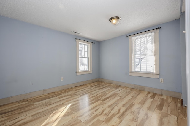 spare room featuring a healthy amount of sunlight, a textured ceiling, and light wood-type flooring