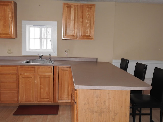 kitchen with sink, light wood-type flooring, kitchen peninsula, and a kitchen bar