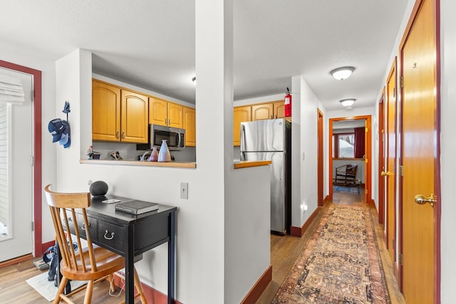 kitchen with appliances with stainless steel finishes, a textured ceiling, and light hardwood / wood-style flooring