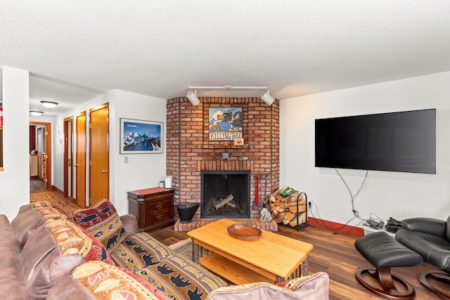 living room featuring wood-type flooring, track lighting, a textured ceiling, and a fireplace