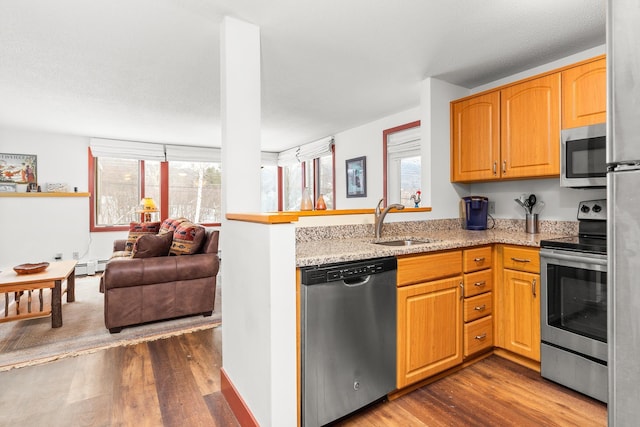 kitchen with dark wood-type flooring, sink, baseboard heating, appliances with stainless steel finishes, and light stone countertops