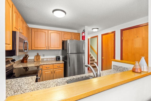 kitchen featuring appliances with stainless steel finishes, sink, light stone counters, and a textured ceiling