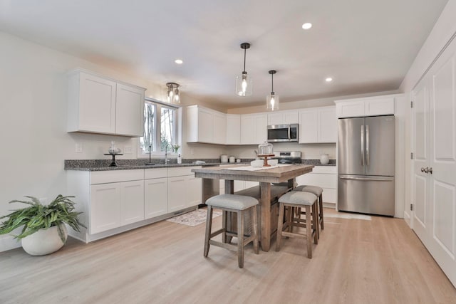 kitchen featuring appliances with stainless steel finishes, dark stone countertops, white cabinets, hanging light fixtures, and light hardwood / wood-style floors