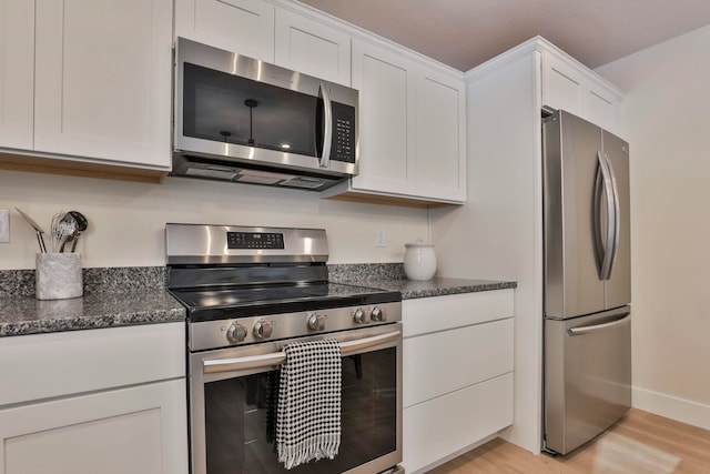 kitchen with appliances with stainless steel finishes, dark stone countertops, white cabinets, and light hardwood / wood-style flooring