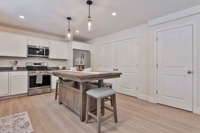 kitchen with light hardwood / wood-style flooring, a kitchen breakfast bar, pendant lighting, stainless steel appliances, and white cabinets