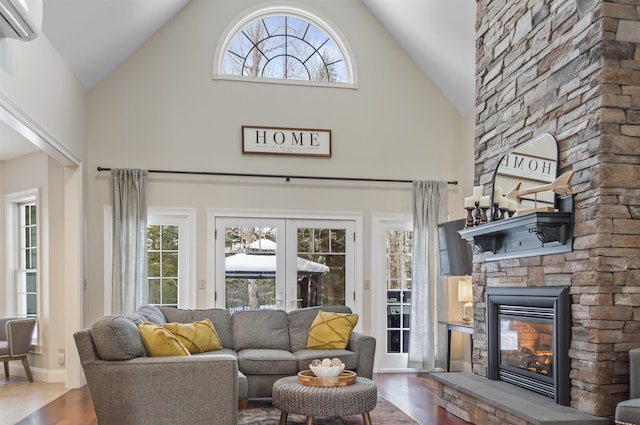 living room with an AC wall unit, high vaulted ceiling, a fireplace, hardwood / wood-style flooring, and french doors