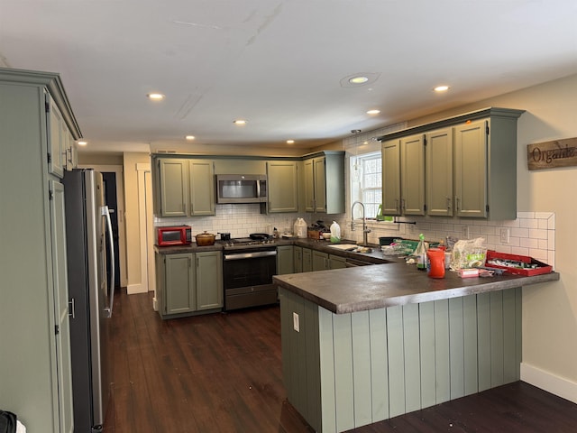 kitchen with a sink, dark countertops, dark wood-style floors, appliances with stainless steel finishes, and a peninsula