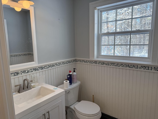 half bathroom with a wainscoted wall, toilet, and vanity