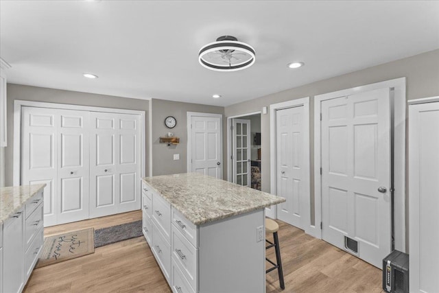 kitchen featuring light stone counters, light hardwood / wood-style floors, a kitchen island, and white cabinets