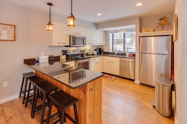 kitchen with white cabinetry, kitchen peninsula, dark stone counters, appliances with stainless steel finishes, and a breakfast bar area