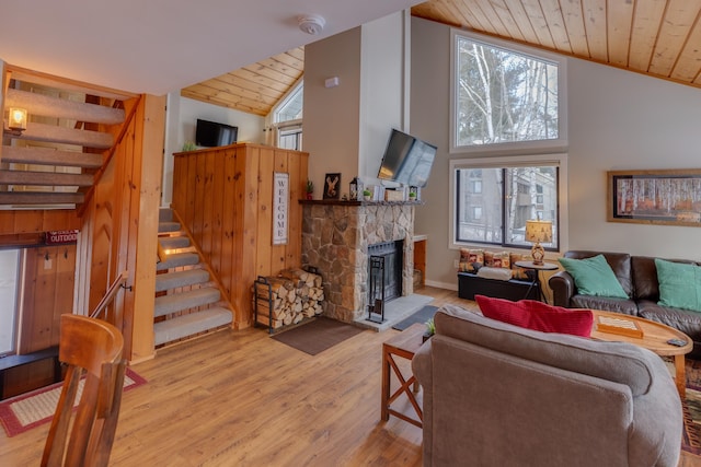 living room with light hardwood / wood-style floors, high vaulted ceiling, wood ceiling, and a stone fireplace