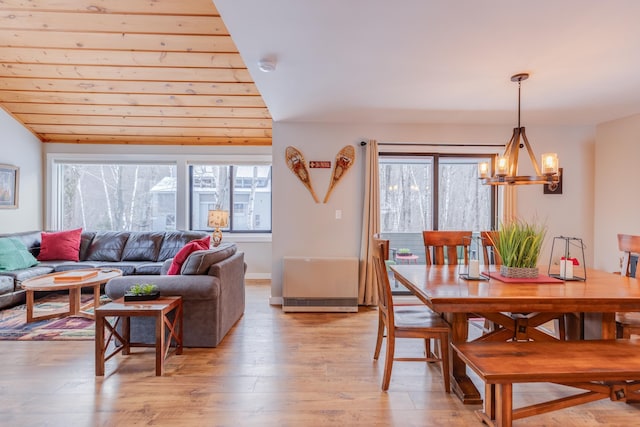 dining space with light wood-type flooring, vaulted ceiling, an inviting chandelier, and a wealth of natural light