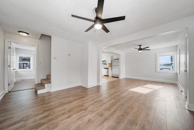 unfurnished living room with a textured ceiling, light hardwood / wood-style flooring, and ceiling fan