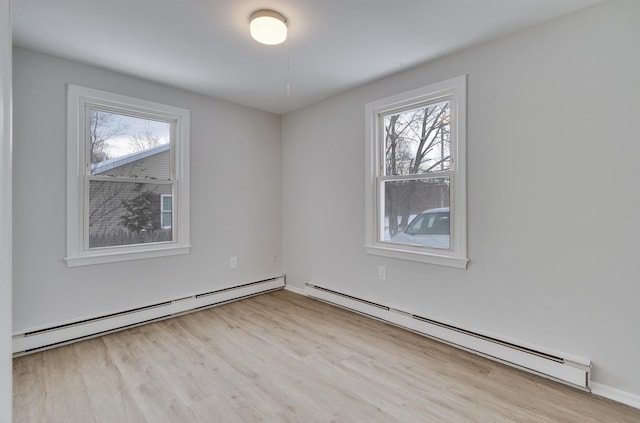 spare room featuring baseboard heating and light hardwood / wood-style floors