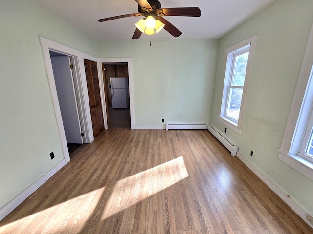 unfurnished bedroom featuring ceiling fan, hardwood / wood-style floors, white fridge, and a baseboard heating unit