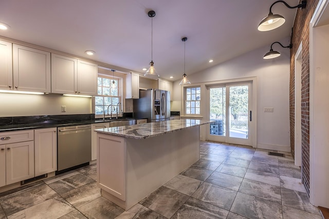 kitchen with lofted ceiling, sink, a center island, dark stone countertops, and appliances with stainless steel finishes