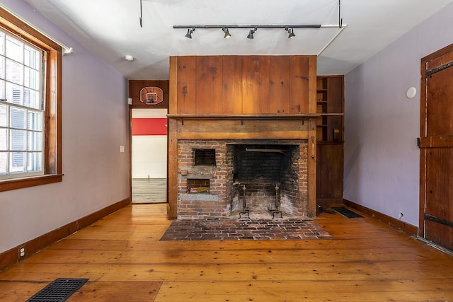 unfurnished living room with a brick fireplace, plenty of natural light, and hardwood / wood-style floors