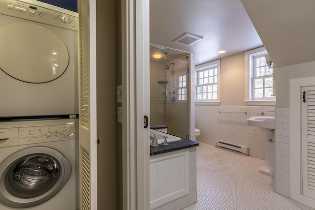 laundry room with light tile patterned flooring, stacked washer and clothes dryer, sink, tile walls, and baseboard heating