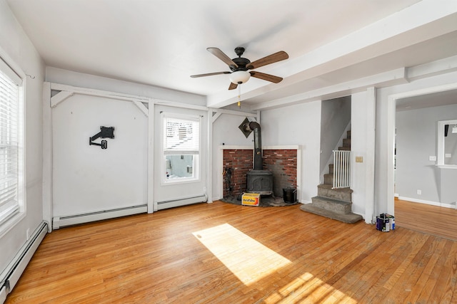 unfurnished living room featuring ceiling fan, a wood stove, baseboard heating, and light hardwood / wood-style floors