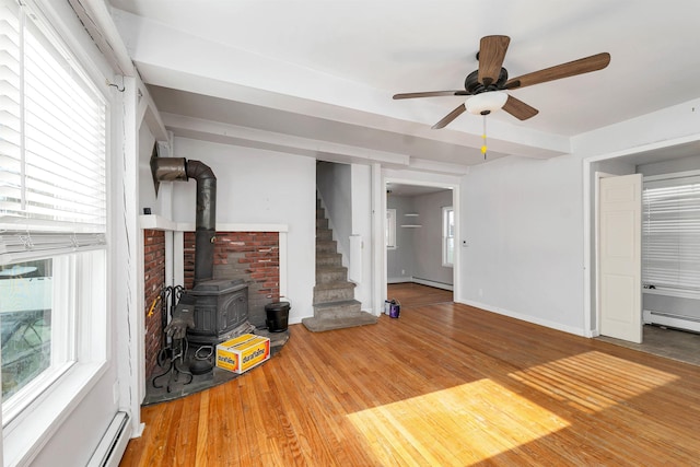 unfurnished living room with hardwood / wood-style flooring, a baseboard heating unit, a wood stove, and ceiling fan