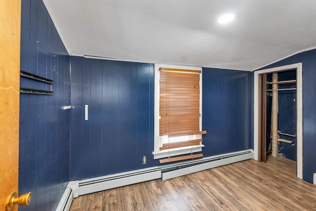 unfurnished bedroom featuring wood walls, hardwood / wood-style flooring, a closet, and baseboard heating