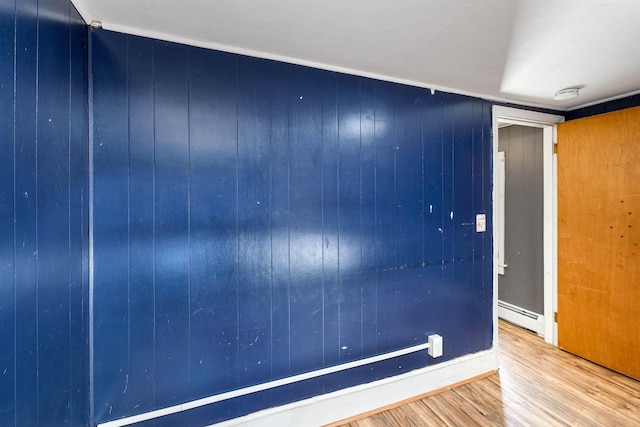 empty room featuring a baseboard heating unit, wooden walls, and hardwood / wood-style floors