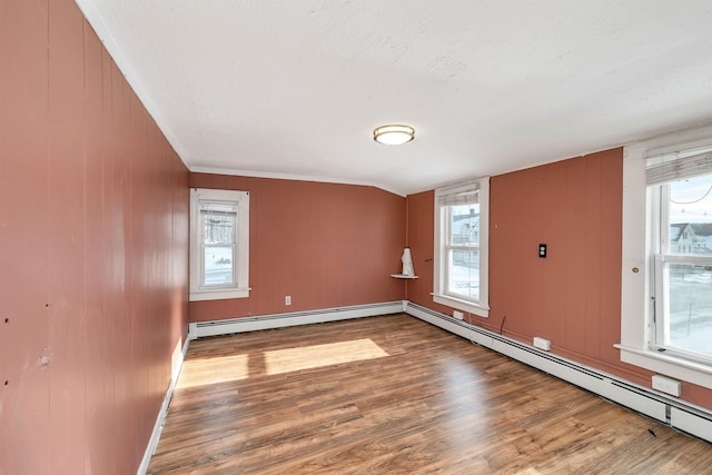 empty room featuring a baseboard heating unit, plenty of natural light, and hardwood / wood-style floors