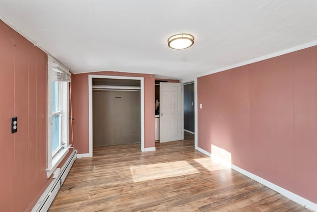 unfurnished bedroom with baseboard heating, wood-type flooring, and wooden walls