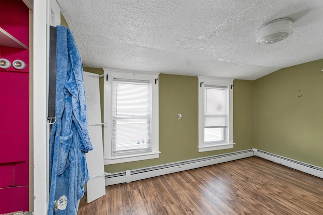 empty room featuring lofted ceiling, a baseboard heating unit, hardwood / wood-style floors, and a textured ceiling