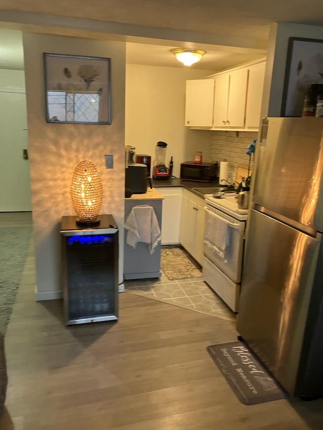 kitchen with white cabinetry, light hardwood / wood-style floors, stainless steel refrigerator, and white range with electric cooktop