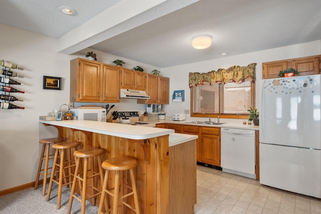 kitchen featuring sink, white appliances, kitchen peninsula, and a kitchen bar