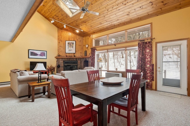 carpeted dining space with wood walls, a skylight, wooden ceiling, track lighting, and a fireplace