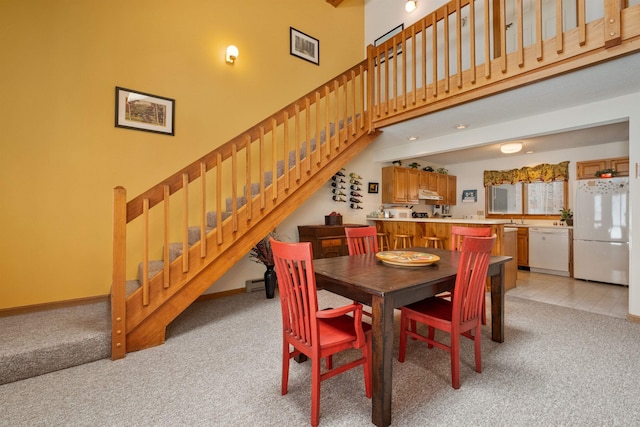 dining area with a high ceiling, a baseboard radiator, and light carpet