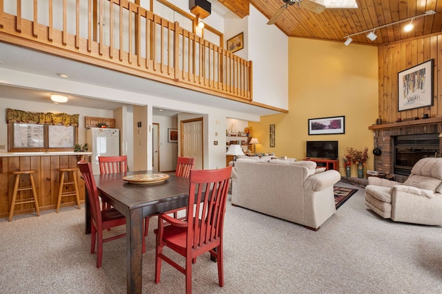 carpeted dining space featuring wood ceiling, a skylight, wooden walls, a high ceiling, and a fireplace