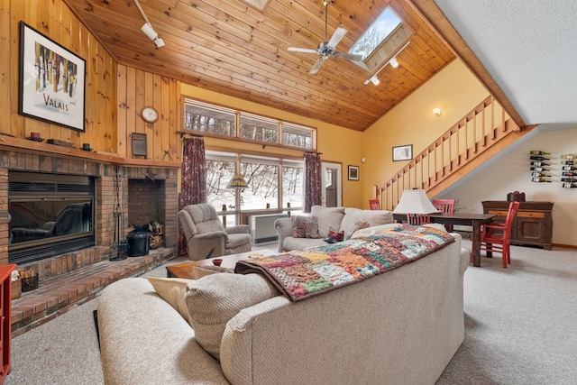 carpeted living room featuring high vaulted ceiling, wooden walls, a skylight, wood ceiling, and a brick fireplace