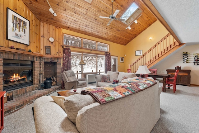 carpeted living room featuring a skylight, wooden walls, high vaulted ceiling, a brick fireplace, and wooden ceiling