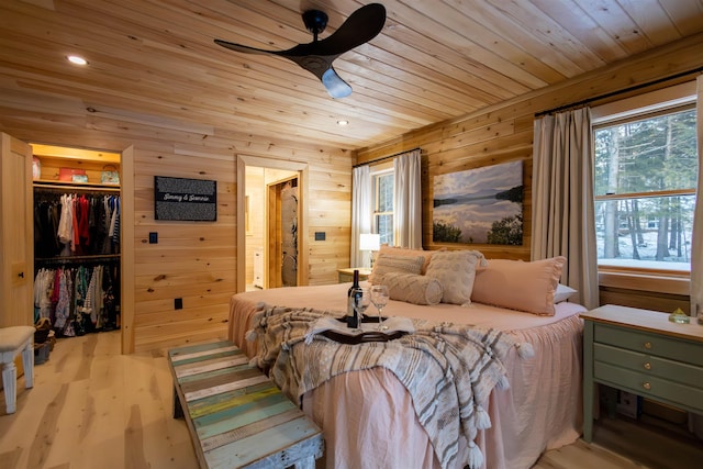 bedroom with wood walls, a walk in closet, ceiling fan, light wood-type flooring, and a closet